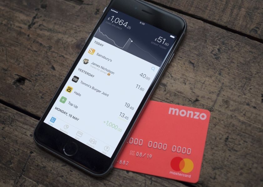 Hot coral Monzo card and iPhone with the Monzo app open.